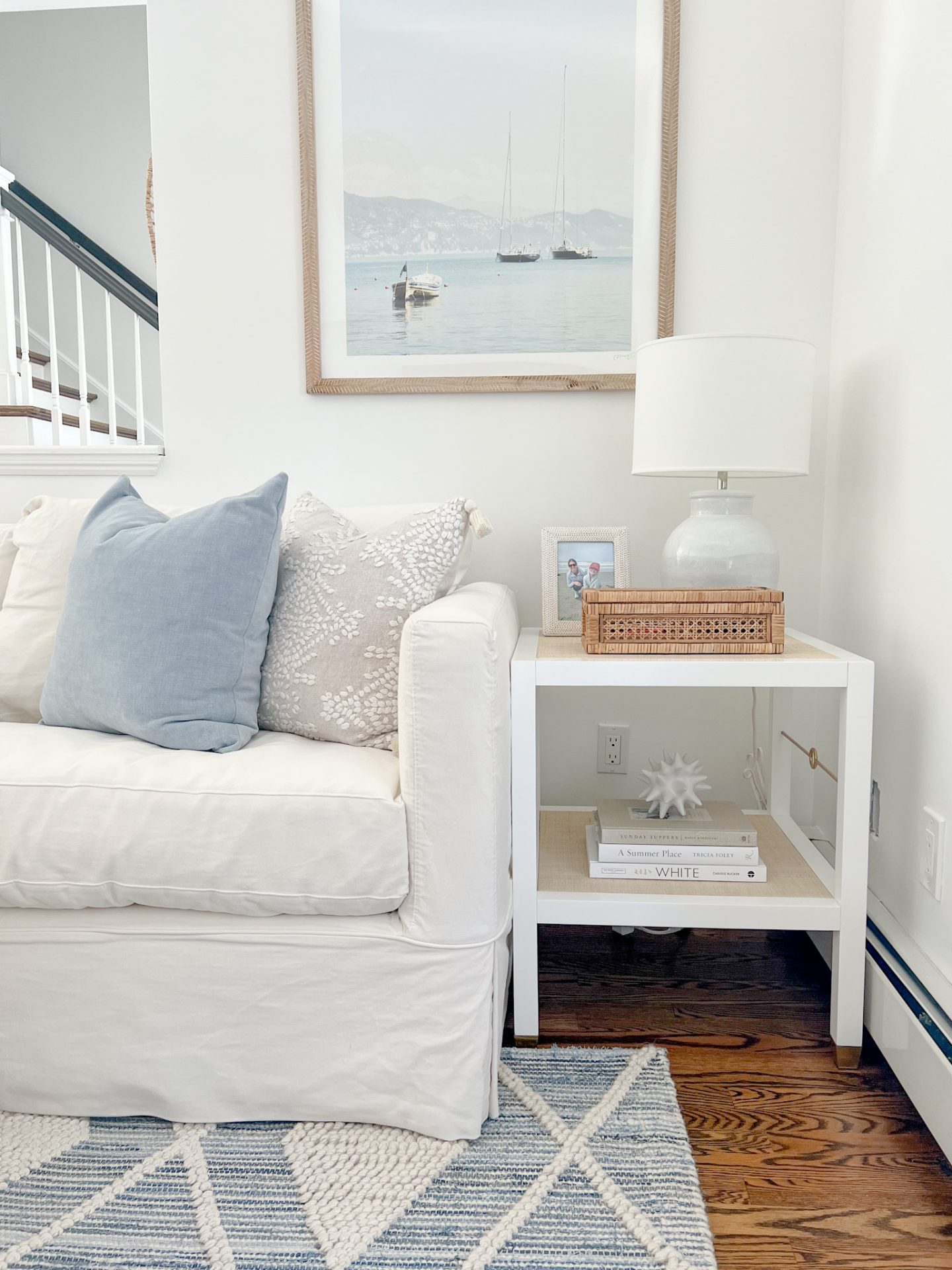 living room with white sofa, blue rug, side table and sailboat artwork