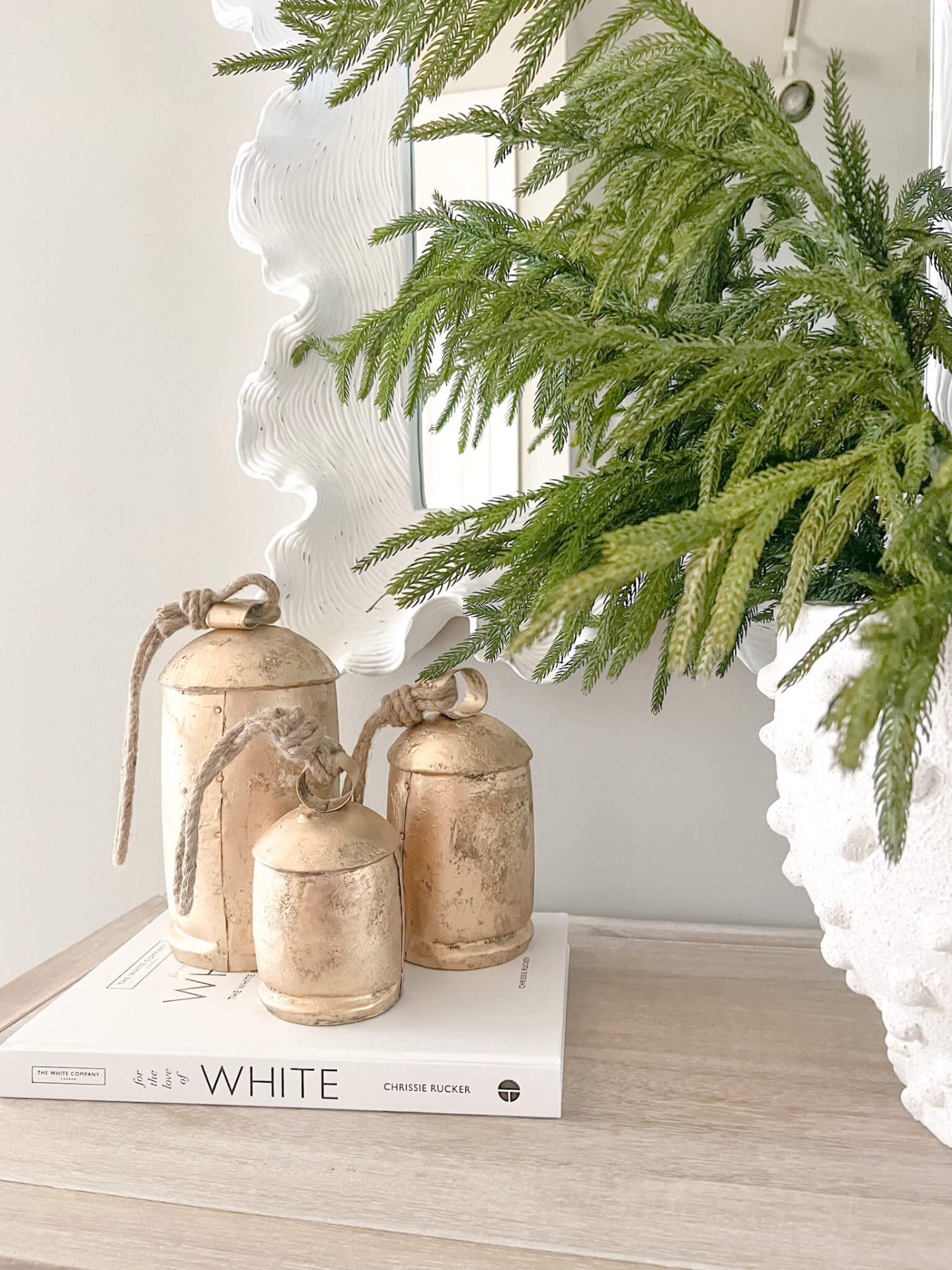 gold christmas bells on top of books with white mirror behind it