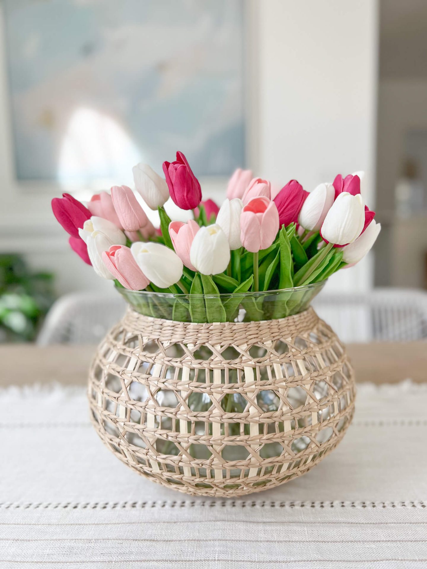 woven vase of pink, red and white tulips on top of a wood dining room table