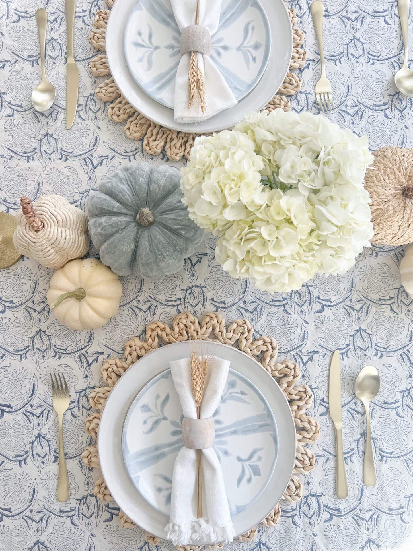 birds eye view of woven plate charger and white plate stacked with white and blue coastal plate with pumpkins on the centerpiece