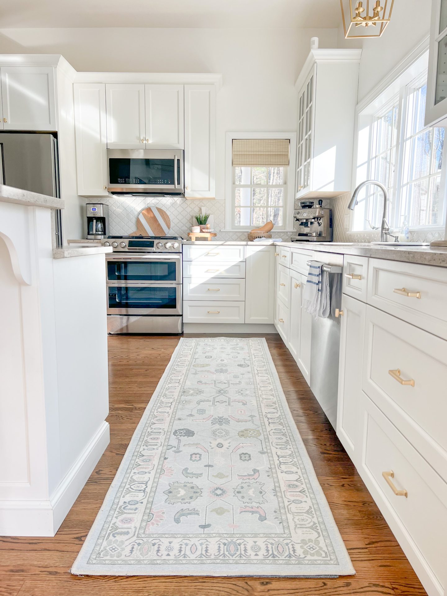 white coastal kitchen with a runner, woven shades & a gold pendant light