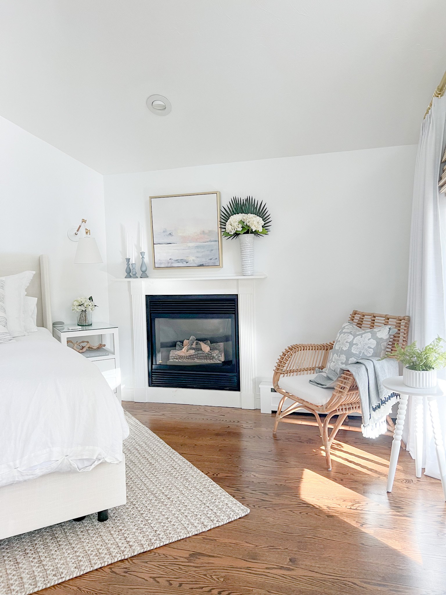 Minimalistic coastal bedroom with neutral rug, white bedding and a rattan chair